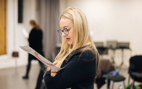 A teacher with blonde hair reading a sheet of paper